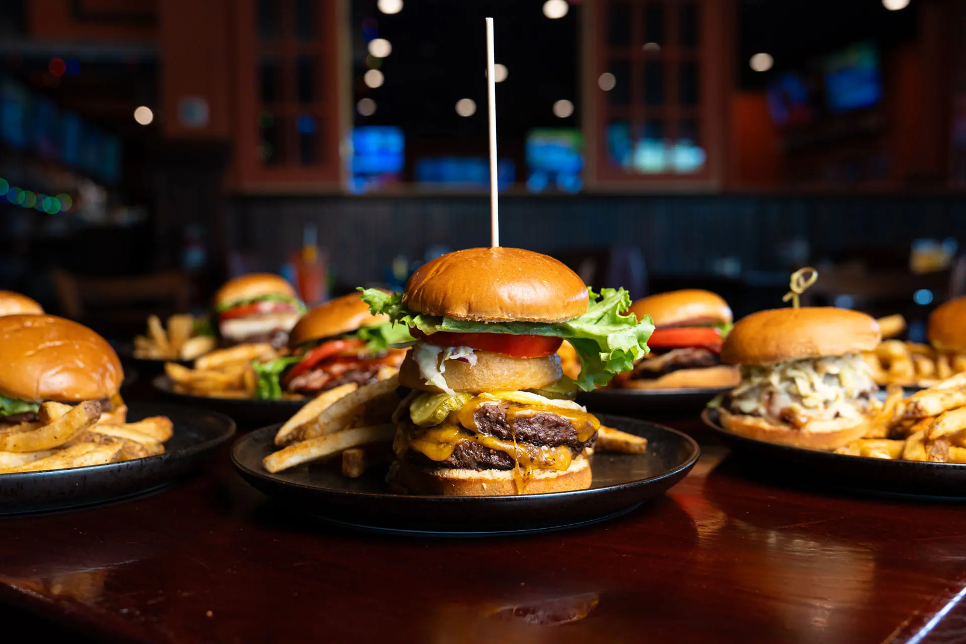 A loaded cheeseburger on a table at Roadhouse, the bar and its screens glowing behind it